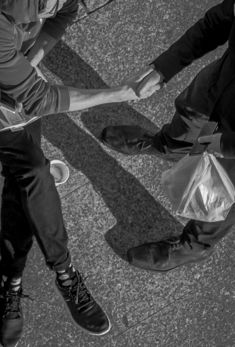 Overhead view of two people shaking hands across sunlit pavement